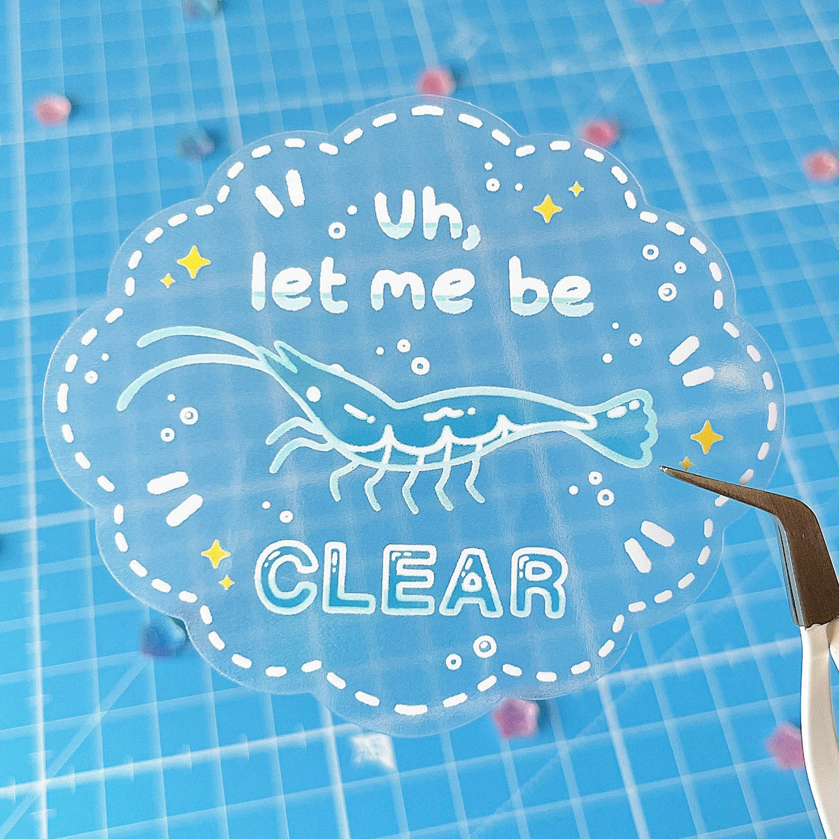 A clear sticker with a shrimp at the centre. The sticker has a white dotted border, yellow stars and white effects, and it has white text that reads "Uh, let me be CLEAR".