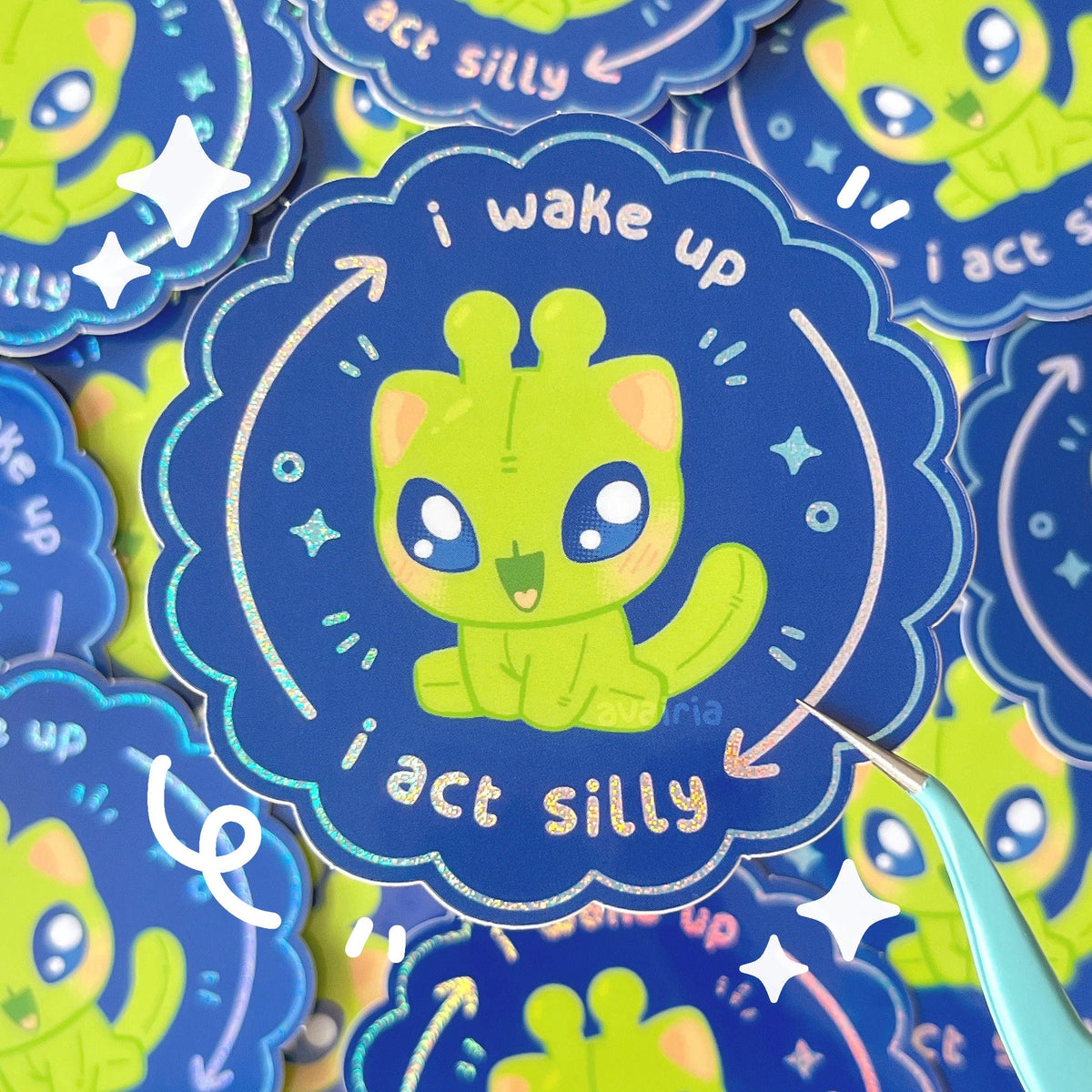 A darker blue sticker with a green alien cat in the centre. The top it reads "i wake up" and an arrow curves to the bottom to text that reads "i act silly", another arrow leads back up to the previous text which all have a holo pixie dust effect.