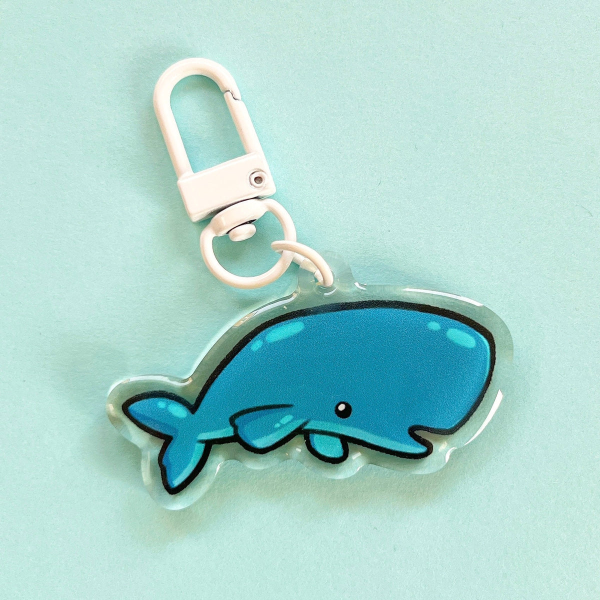 An acrylic charm of a sperm whale, it has a white clasp accessory.