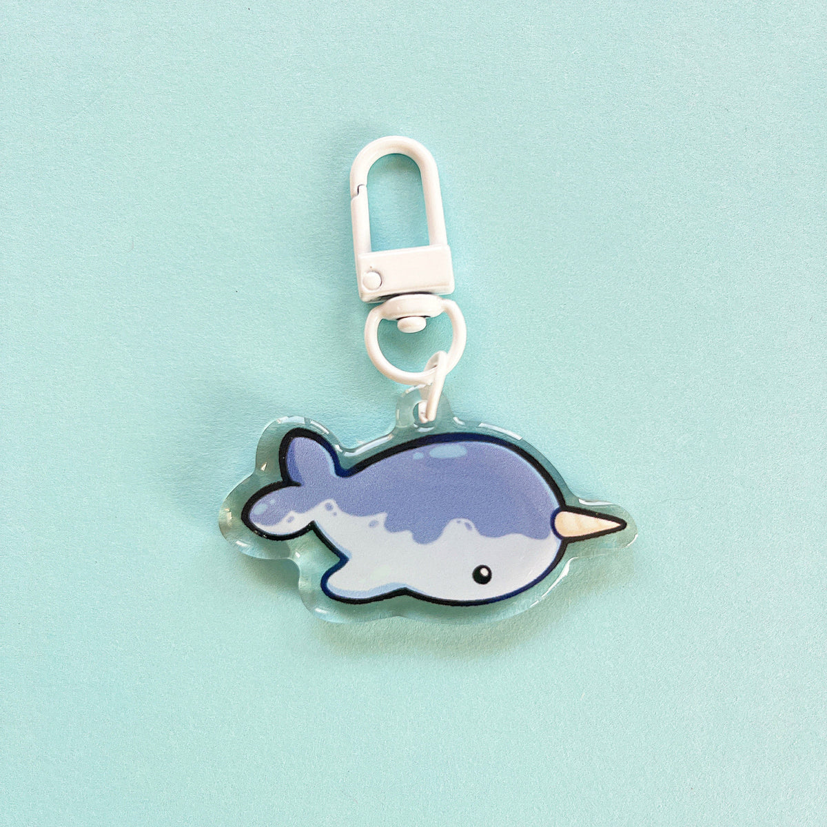 An acrylic charm of a narwhal, it has a white clasp accessory.