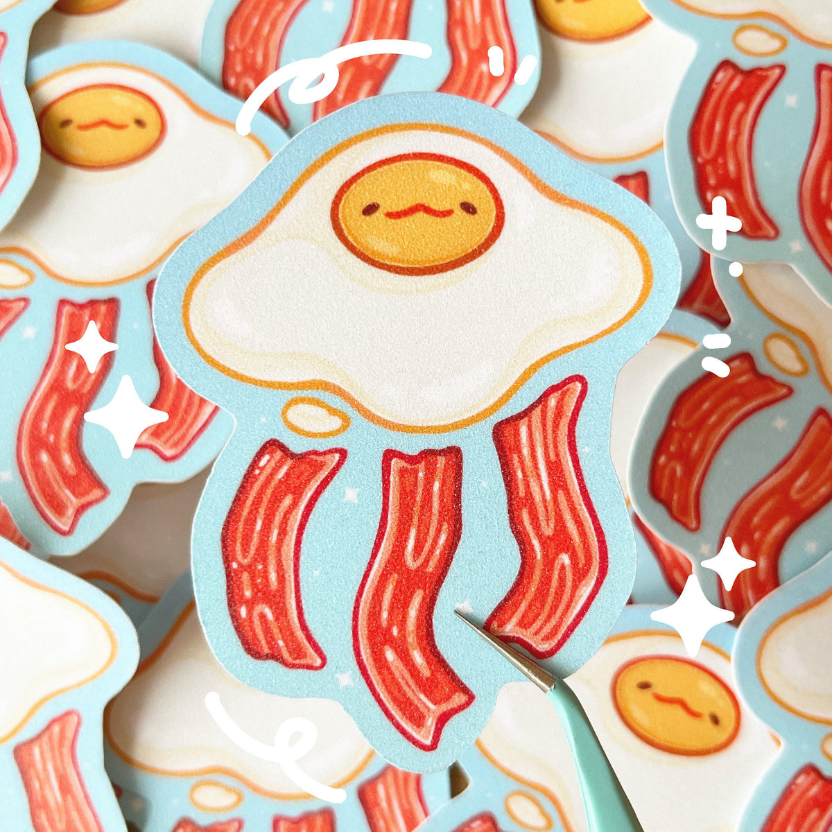 A glitter textured sticker of an egg and bacon themed jellyfish on a blue background.