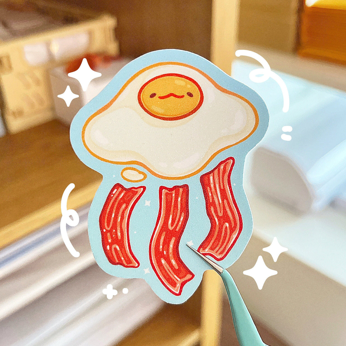 A glitter textured sticker of an egg and bacon themed jellyfish on a blue background.