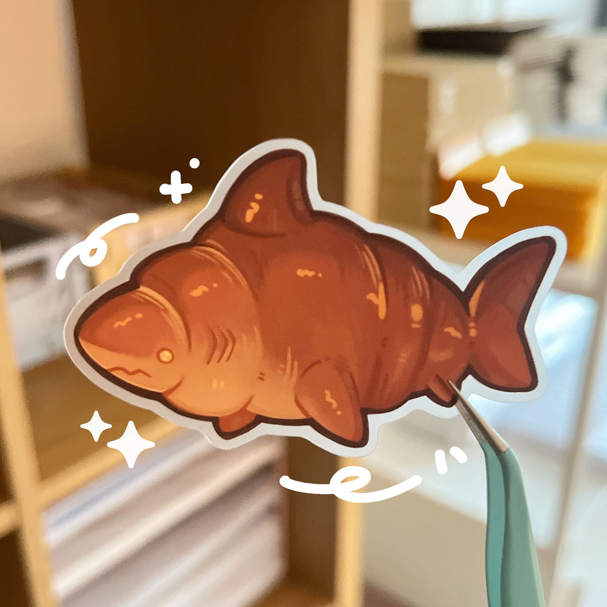 A sticker of a brown croissant shark, the background of the sticker is a matte clear effect.