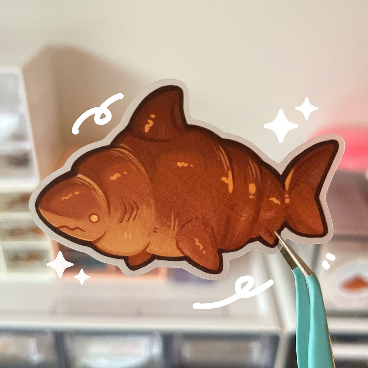A sticker of a brown croissant shark, the background of the sticker is a matte clear effect.