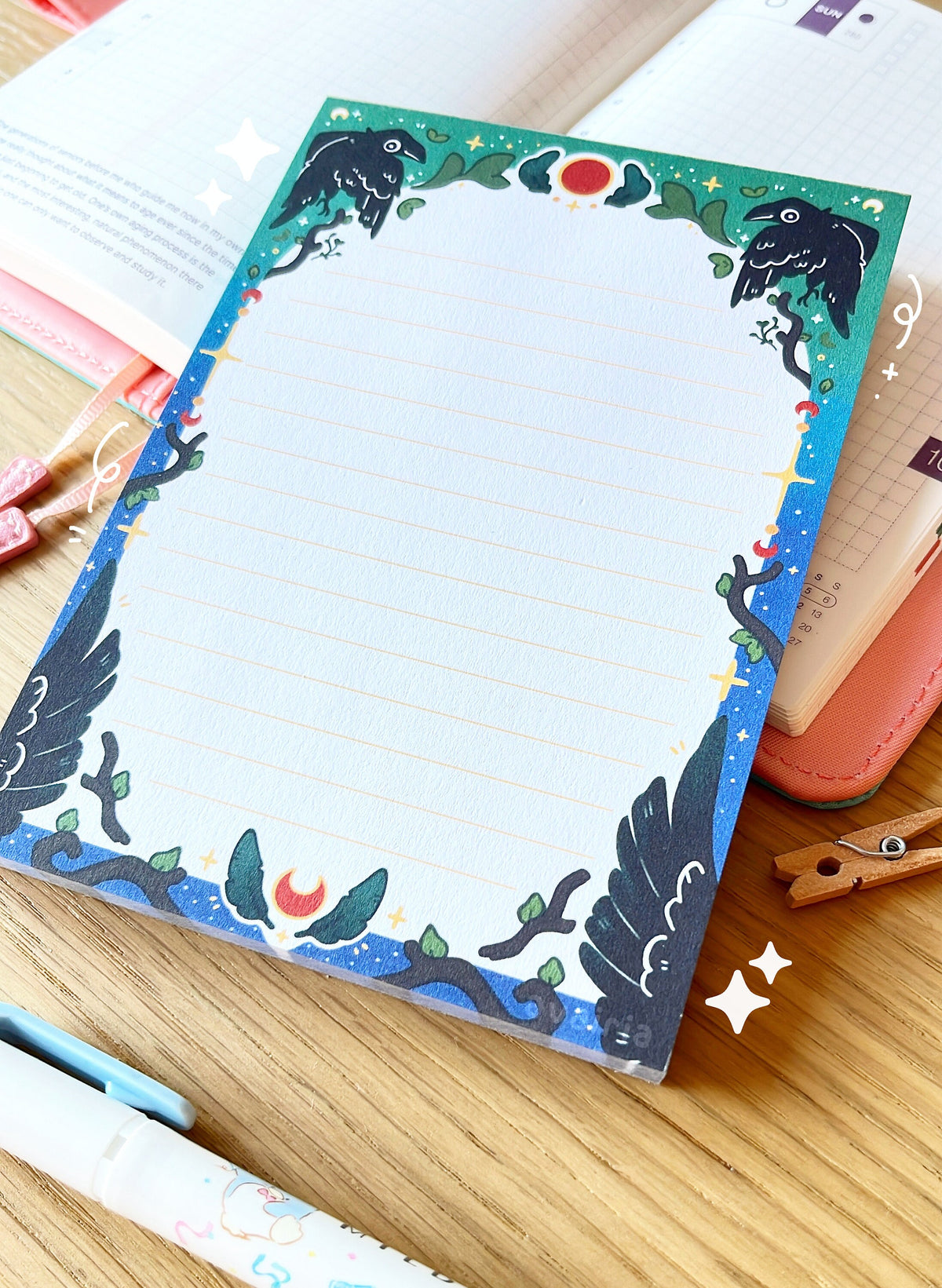 The notepad has an arched green to blue border with a crow, feather and twig design with small star details. The inside of the border is white with small yellow lines.