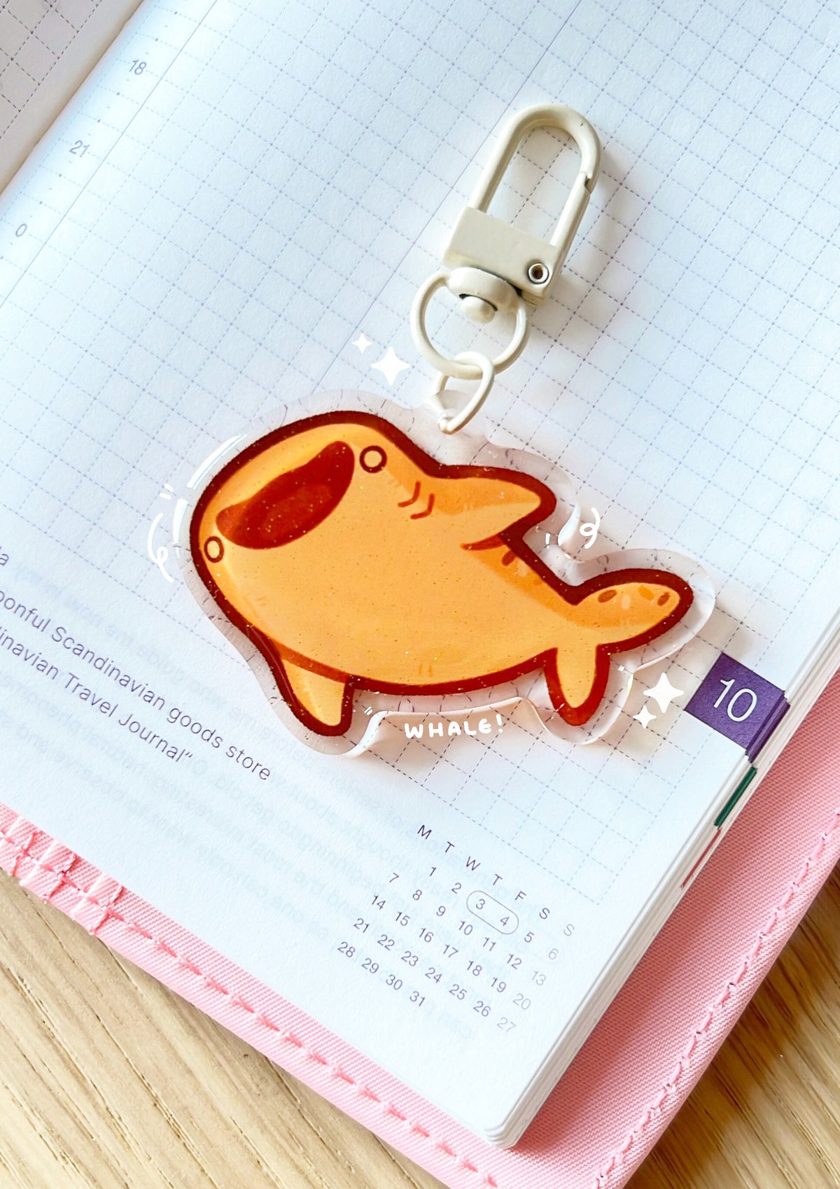 An acrylic charm of a bread whale shark with a gold glitter effect. The charm has a beige clasp accessory.