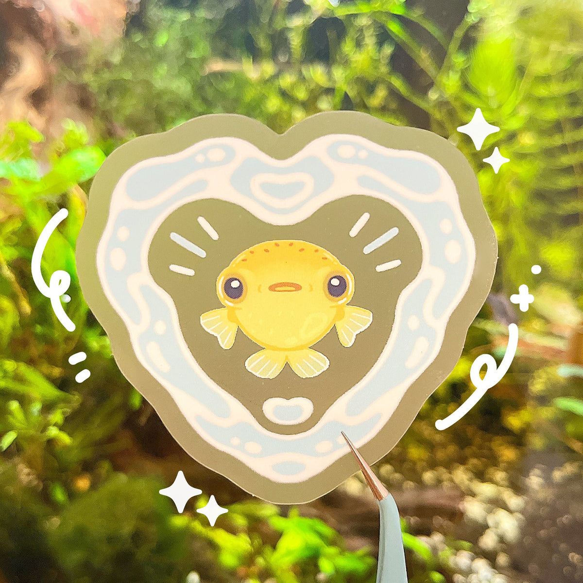 The sticker has a small yellow pufferfish at the centre, with a heart made out of water surrounding it. The design is on a matte clear background.