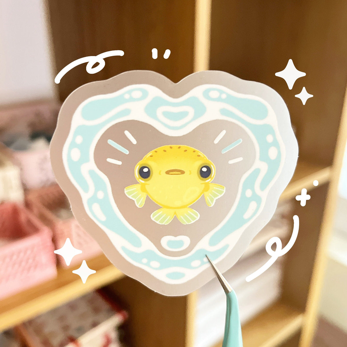 The sticker has a small yellow pufferfish at the centre, with a heart made out of water surrounding it. The design is on a matte clear background.
