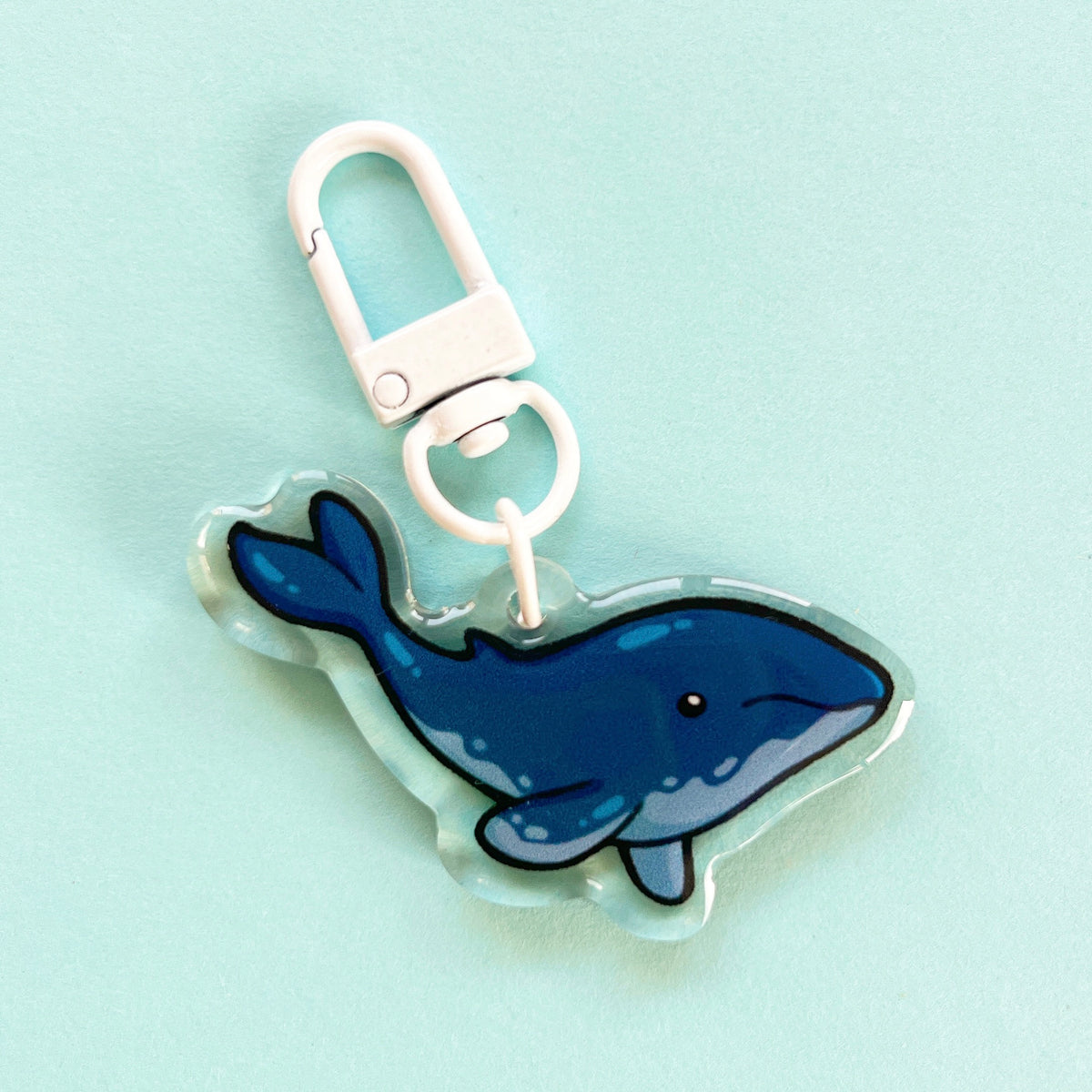 An acrylic charm of a humpback whale, it has a white clasp accessory.
