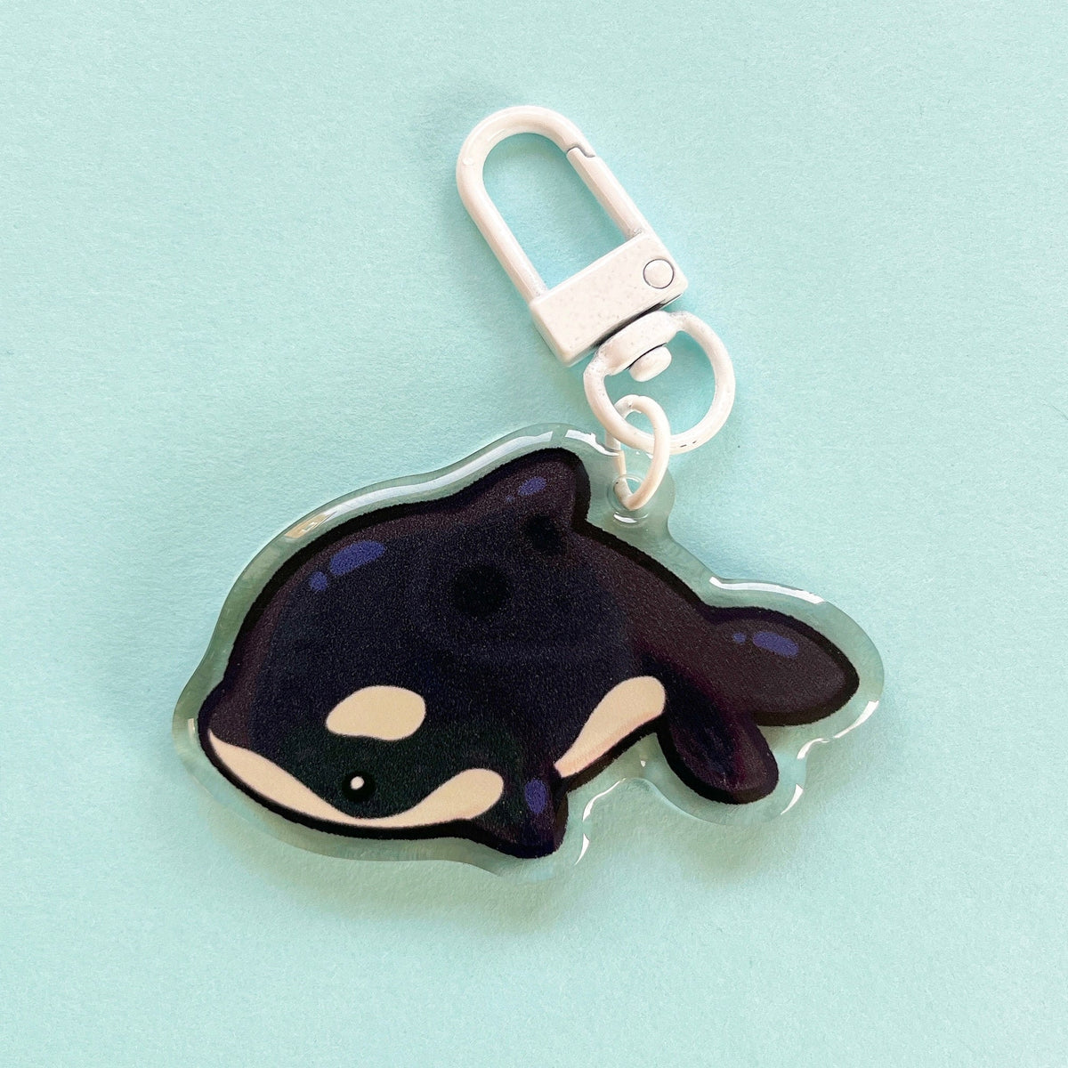 An acrylic charm of an orca, it has a white clasp accessory.