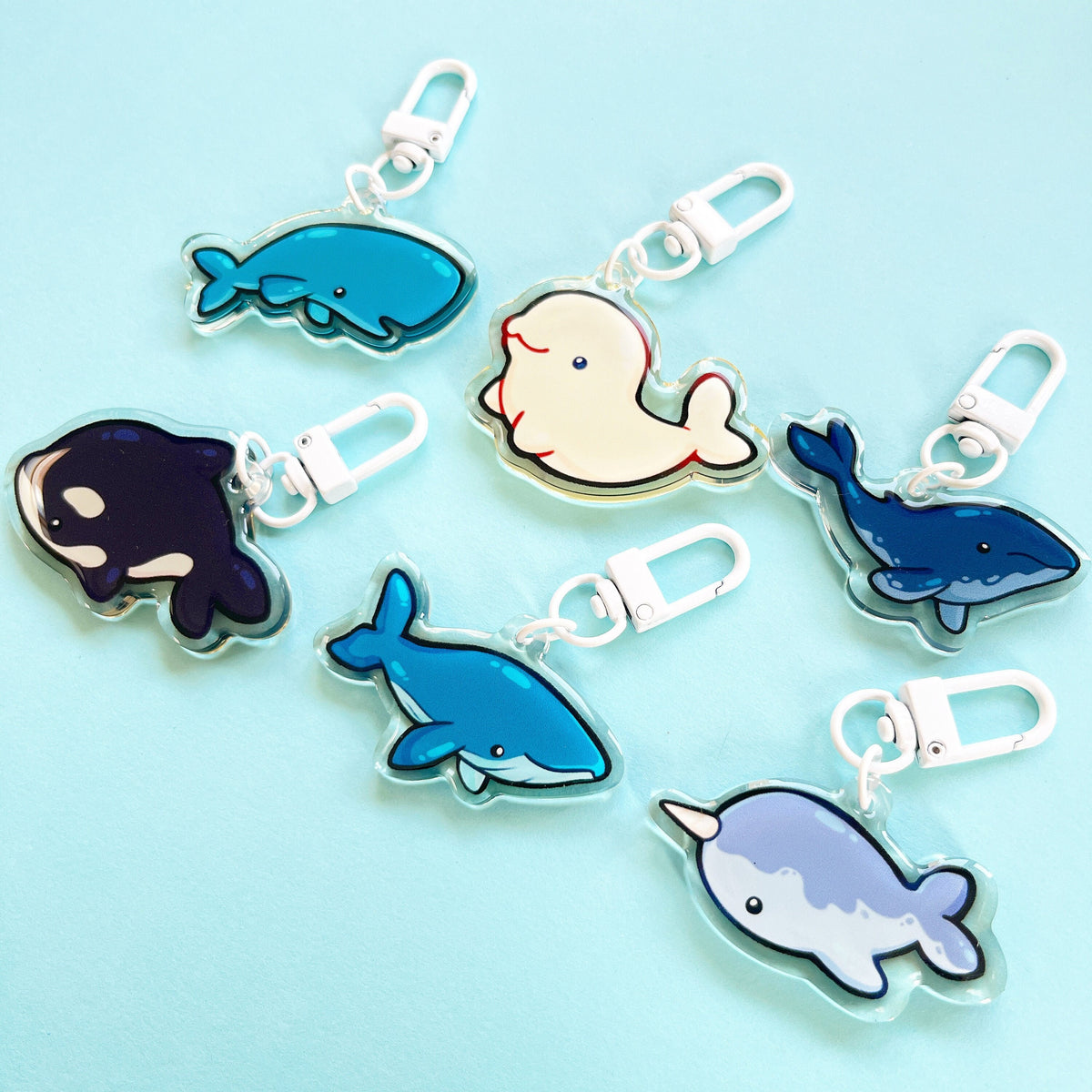A set of different whale acrylic charm designs with white clasp accessories. From top left to bottom right - sperm whale, beluga whale, humpback whale, orca, blue whale and a narwhal.