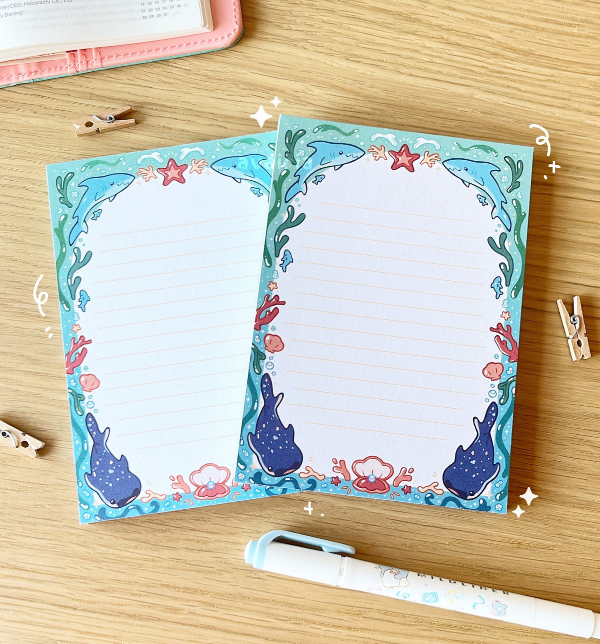 The notepads have an arched blue border with a shark and underwater design with small star and bubble details. The inside of the border is white with small yellow lines.