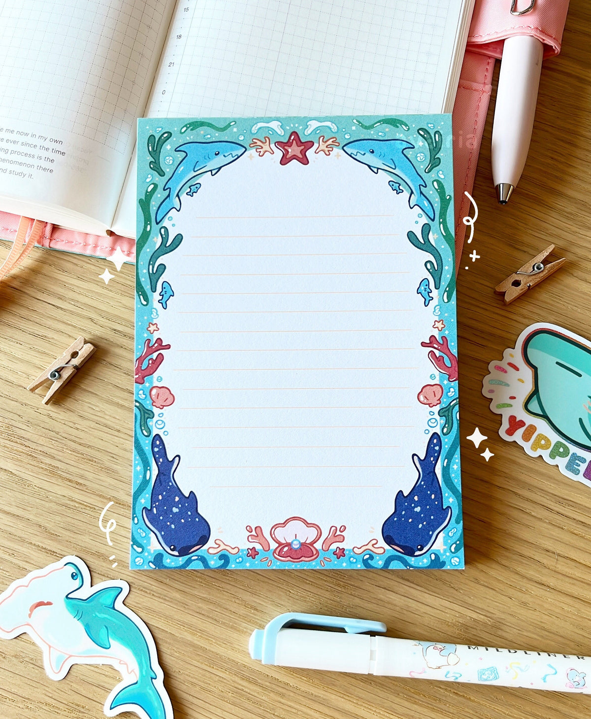 The notepad has an arched blue border with a shark and underwater design with small star and bubble details. The inside of the border is white with small yellow lines.