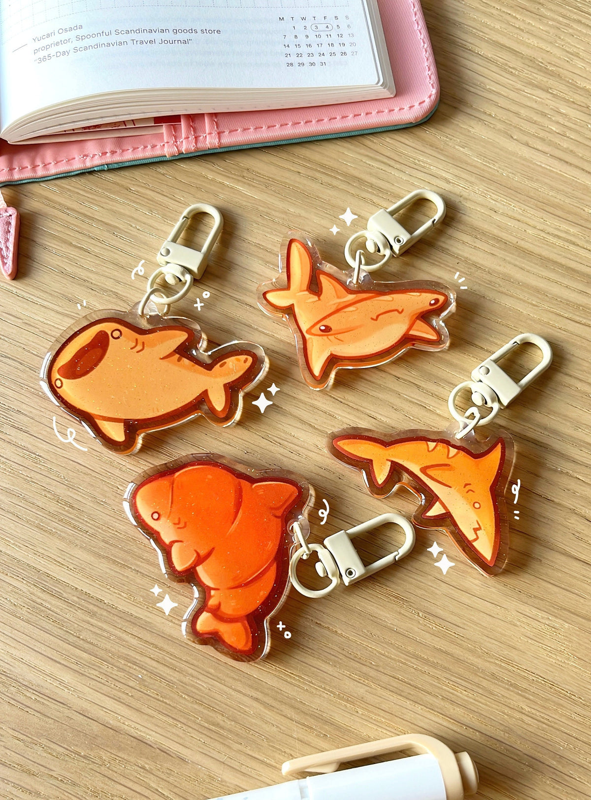 4 different acrylic charms of bread sharks, each have a beige coloured clasp accessory. The charms have a gold glitter effect in the epoxy.